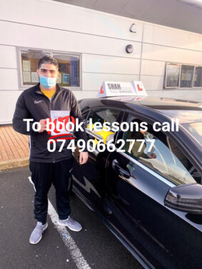 a man wearing a face mask standing next to a car outside of a Driving School in Bolton.