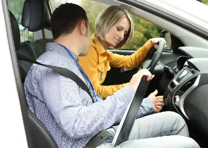 Two people, one man and one woman sitting in the car. Both wearing seat belts. She appears to be adjusting a control on the dashboard while he looks down at the car's interior.