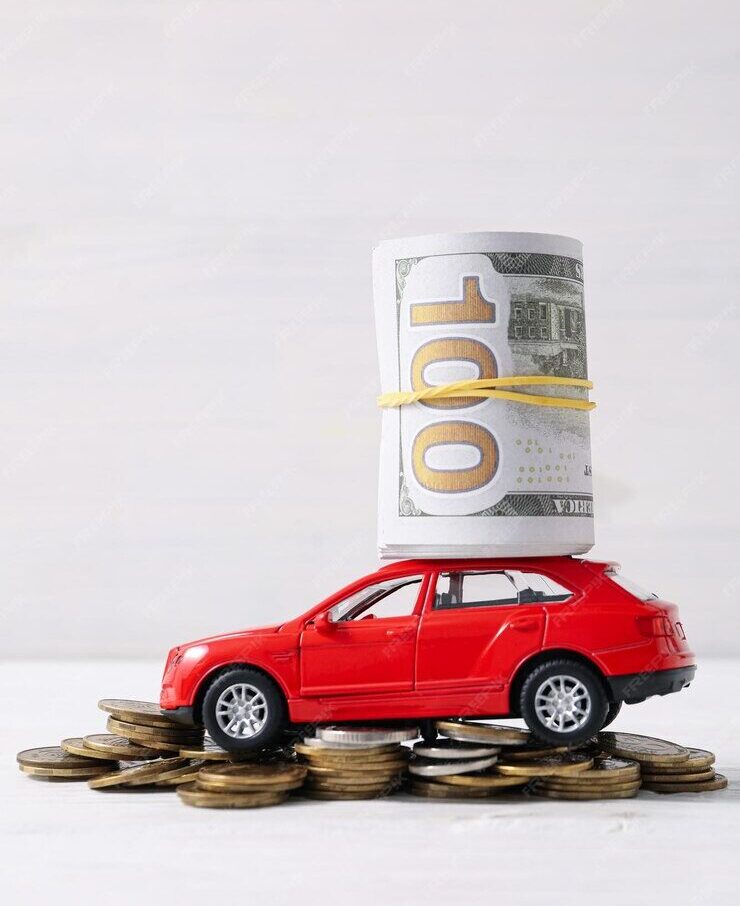 A rolled-up stack of 100-dollar bills and placed on top of a small red toy car. The car is positioned on a pile of coins, symbolizing concepts like car expenses, savings, or financial planning.