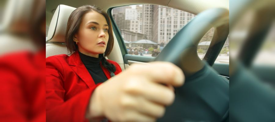 Woman grips the steering wheel of a car with a focused and slightly concerned expression as she takes a driving lesson.
