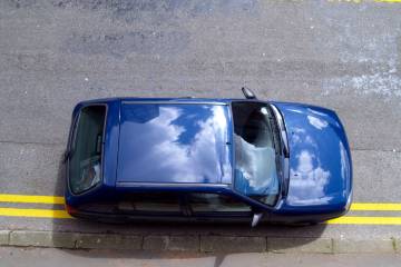Blue car parked on double yellow lines on a UK street, violating parking restrictions.