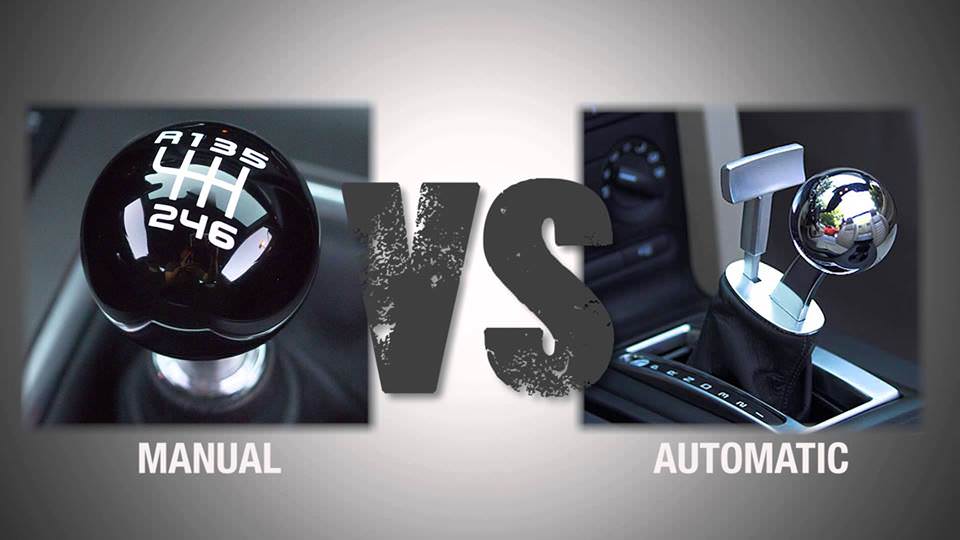 A side-by-side comparison image labeled "MANUAL vs AUTOMATIC." On the left, a close-up shows a classic black spherical manual gear shifter with a 6-speed H-pattern engraved on top. On the right, a modern, polished chrome automatic gear selector is shown in a center console. The "VS" text in the center is styled with a weathered, metallic texture against a neutral grey gradient background.