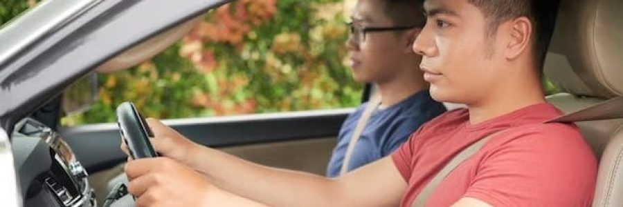 Two persons sitting in the car one woman and one man. A driving instructor is sitting in the passenger seat, instructing a young woman who is focused on steering the car.