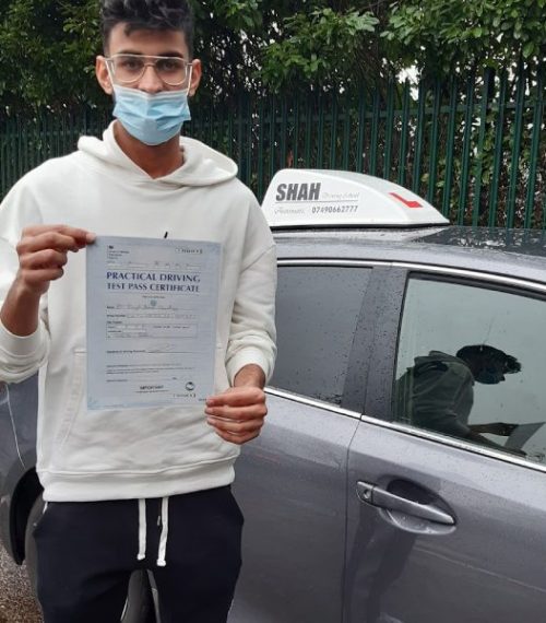 A person wearing glasses and a face mask, holding a Practical Driving Test Pass Certificate in one hand.
